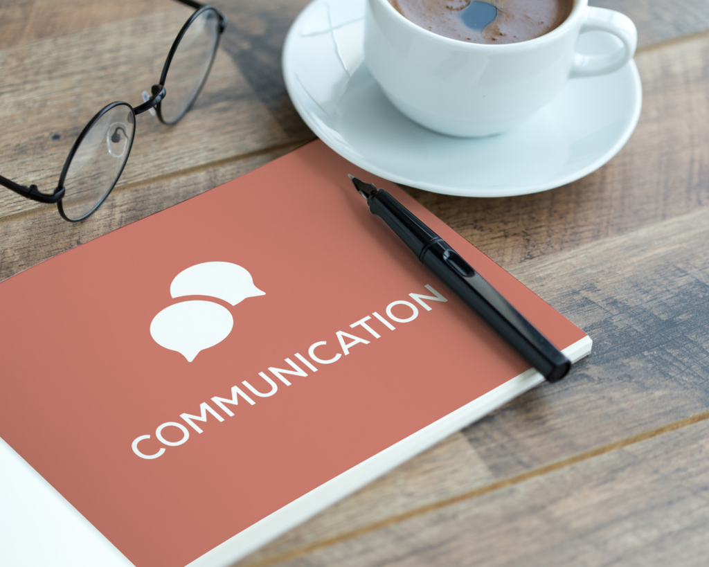a book saying 'Communication' with a pen, glasses and coffee in a mug depicting the importance of communication in the client journey