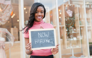 Image of a girl holding a chalkboard saying 'Now Hiring' to depict the cost of hiring an online business manager